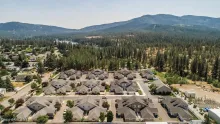 Aerial view of a modern townhome community bordered by pine forests, with a scenic lake and mountains in the background.